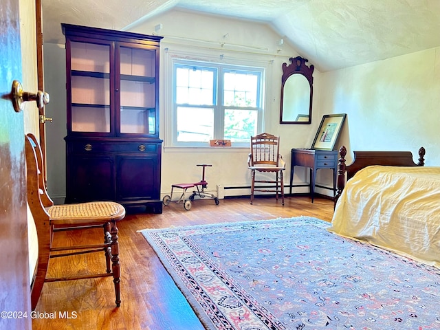 bedroom with wood-type flooring, baseboard heating, a textured ceiling, and lofted ceiling