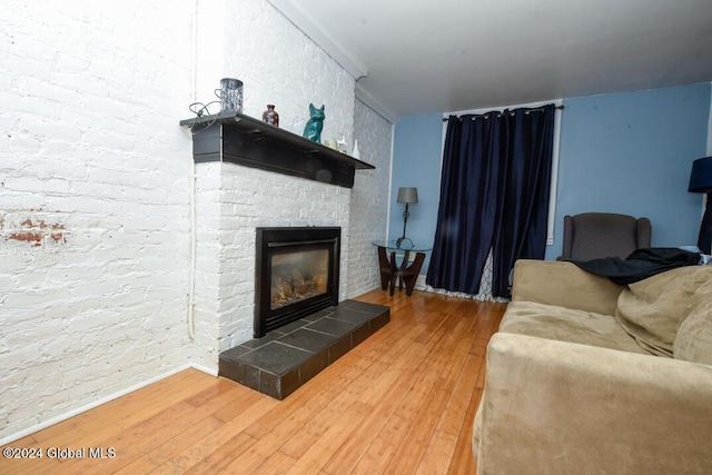 living area with a tiled fireplace, hardwood / wood-style flooring, and brick wall