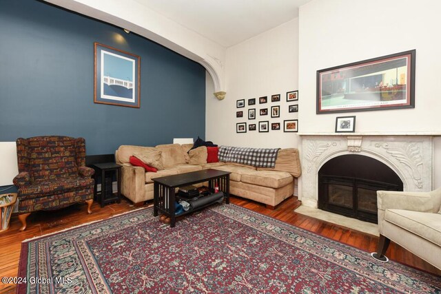 living room featuring a fireplace with flush hearth, arched walkways, and wood finished floors