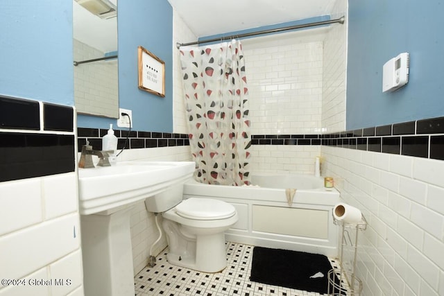 full bath featuring tile patterned floors, toilet, tile walls, wainscoting, and shower / bath combo with shower curtain