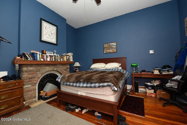 bedroom featuring wood-type flooring, ceiling fan, and a fireplace