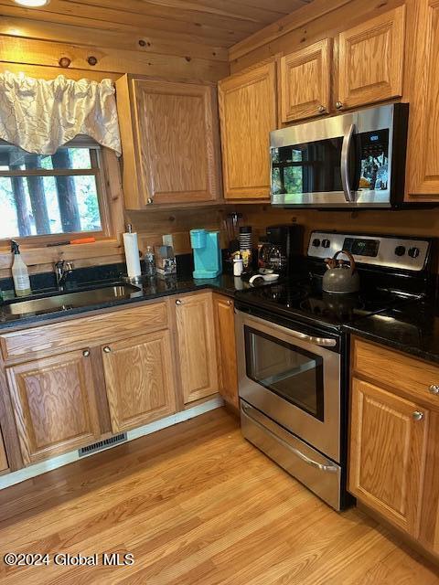 kitchen featuring a sink, visible vents, stainless steel appliances, light wood finished floors, and wooden ceiling