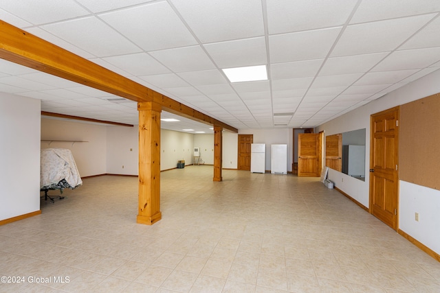 basement with a paneled ceiling and white fridge