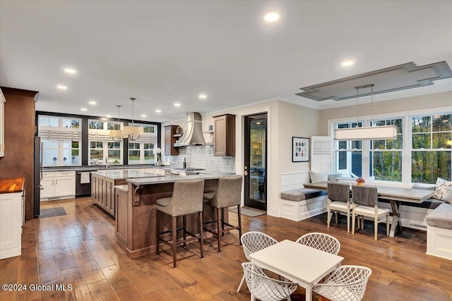 kitchen featuring a kitchen breakfast bar, black dishwasher, freestanding refrigerator, wall chimney range hood, and dark wood-style flooring