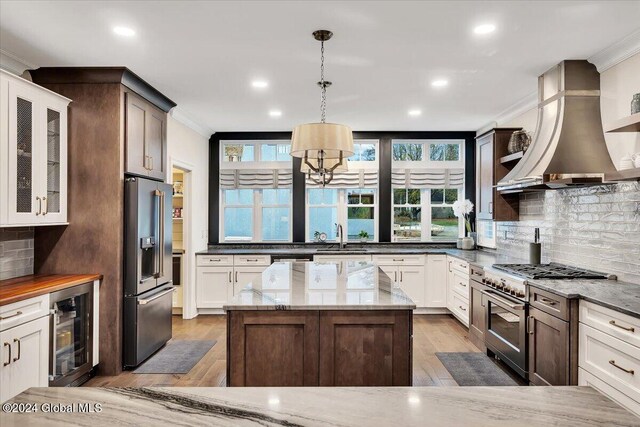 kitchen with wall chimney exhaust hood, beverage cooler, premium appliances, and ornamental molding