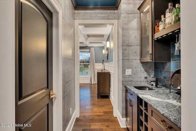 interior space featuring coffered ceiling, dark wood finished floors, a sink, wainscoting, and beamed ceiling