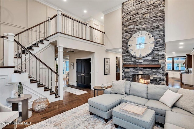 living area with ornamental molding, wood finished floors, stairway, a high ceiling, and a fireplace