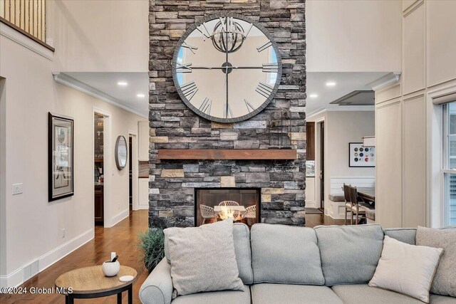 living room featuring crown molding, baseboards, a stone fireplace, a towering ceiling, and wood finished floors