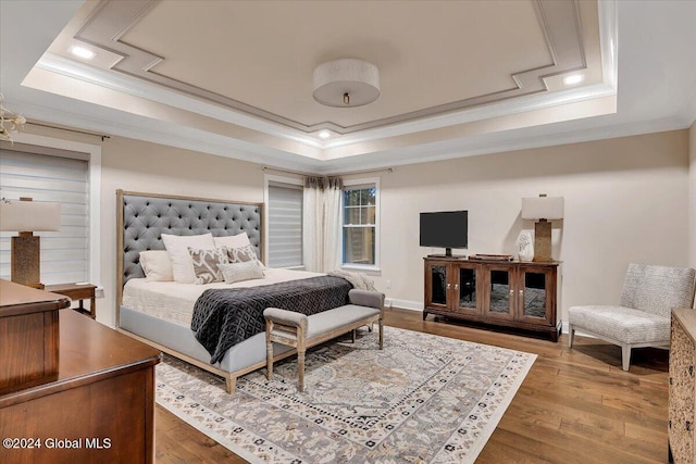 bedroom with a raised ceiling, wood finished floors, and crown molding