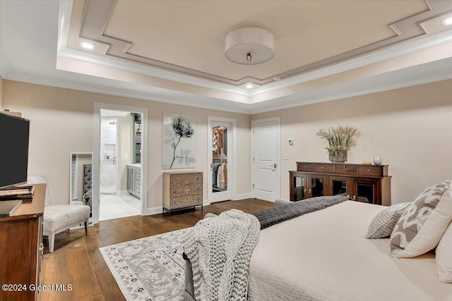 bedroom with hardwood / wood-style floors, a tray ceiling, a walk in closet, and crown molding