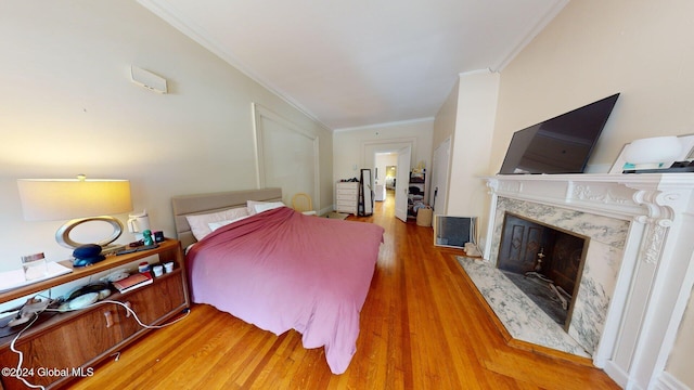 bedroom with wood-type flooring, ornamental molding, and a high end fireplace