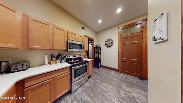 kitchen featuring light brown cabinetry, lofted ceiling, appliances with stainless steel finishes, and dark wood-type flooring