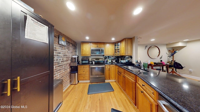 kitchen featuring light hardwood / wood-style floors, brick wall, stainless steel appliances, dark stone counters, and sink