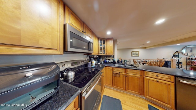 kitchen with light hardwood / wood-style flooring, dark stone countertops, appliances with stainless steel finishes, and sink