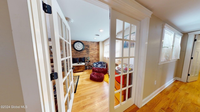 living area with brick wall, light hardwood / wood-style floors, french doors, and a wealth of natural light