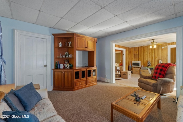 carpeted living room featuring ceiling fan, wooden walls, a paneled ceiling, and heating unit