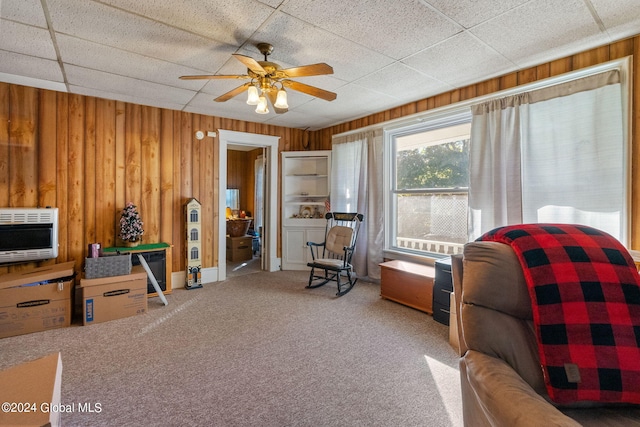 living area with wood walls, carpet floors, a drop ceiling, and ceiling fan