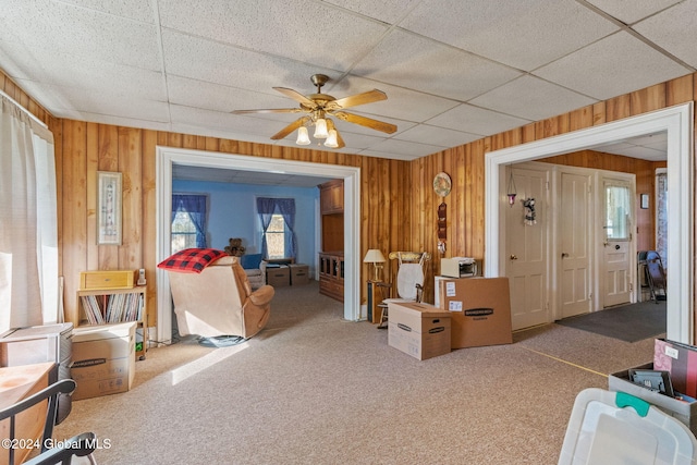 misc room featuring a drop ceiling, ceiling fan, wood walls, and carpet