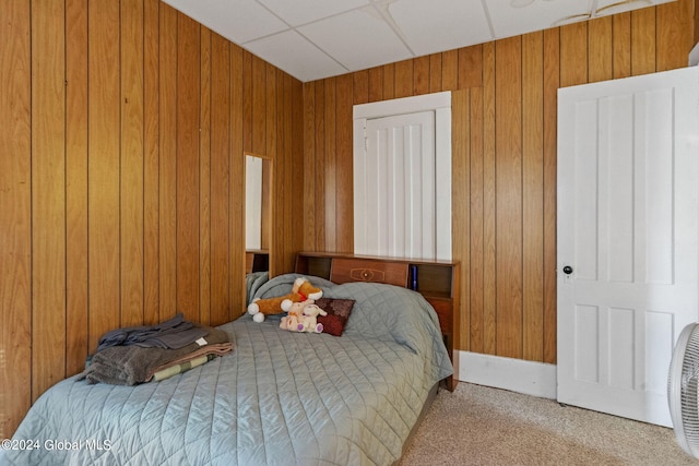 bedroom with a paneled ceiling, light colored carpet, and wooden walls