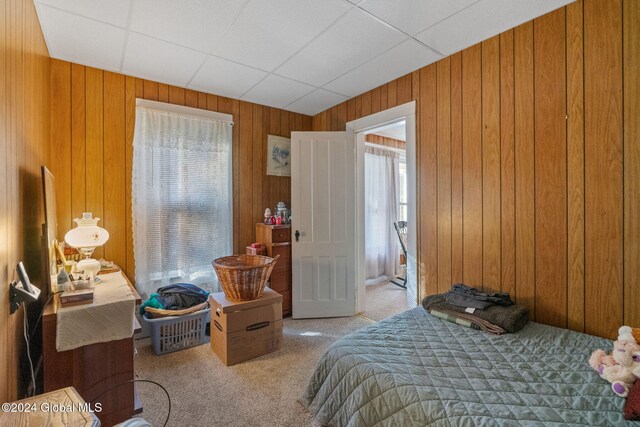 bedroom featuring a drop ceiling, wooden walls, and light carpet