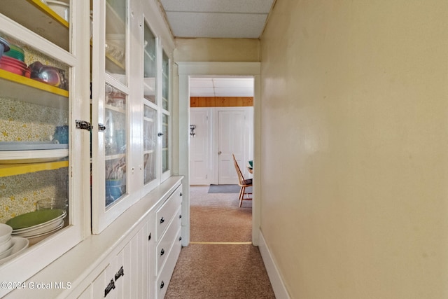 corridor featuring a paneled ceiling and dark carpet