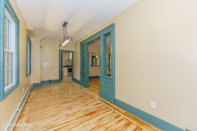 hall with an inviting chandelier, light wood-type flooring, baseboard heating, and ornate columns