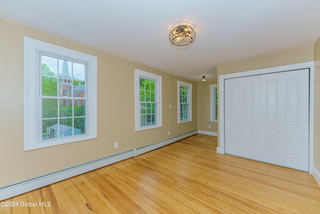 unfurnished bedroom with multiple windows, baseboard heating, light hardwood / wood-style flooring, and a closet