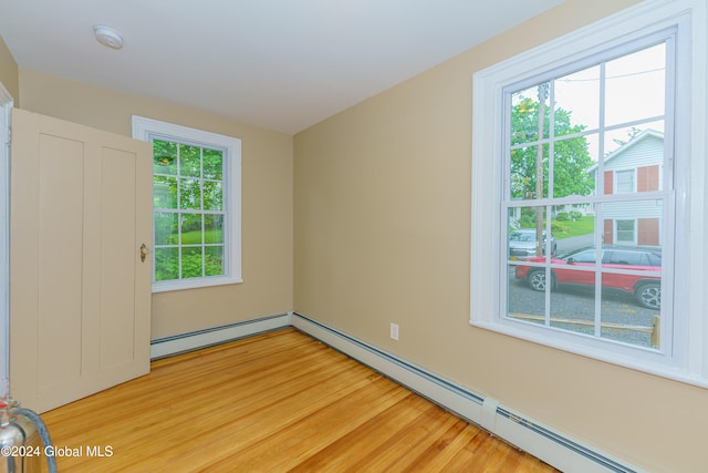 spare room with a baseboard radiator, light wood-type flooring, and a healthy amount of sunlight