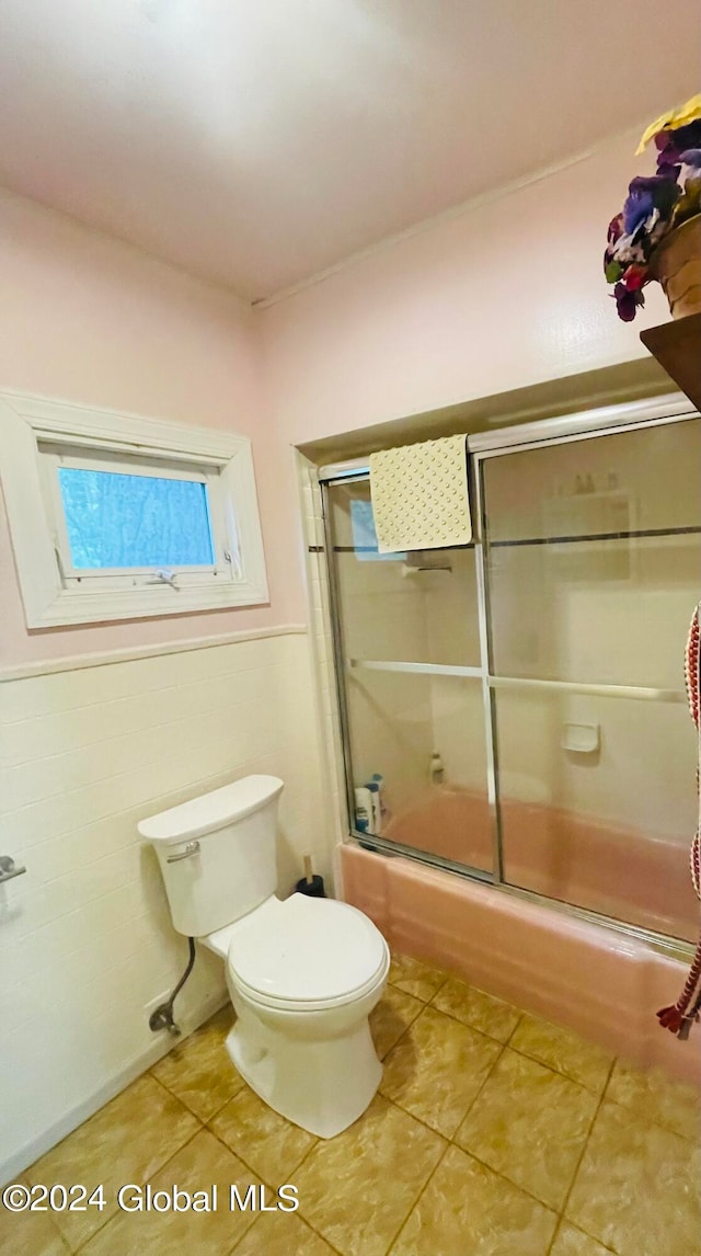 bathroom with combined bath / shower with glass door, tile patterned floors, and toilet