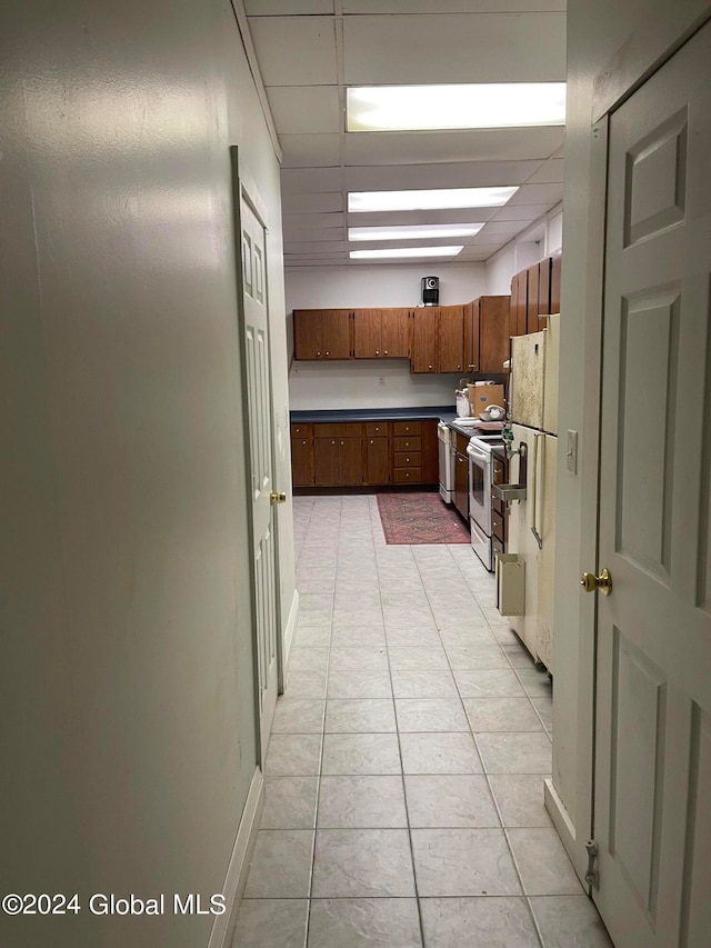 kitchen featuring white appliances, a drop ceiling, and light tile patterned floors