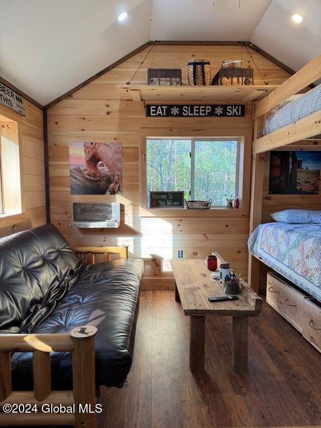 bedroom featuring wooden walls, lofted ceiling, and hardwood / wood-style floors