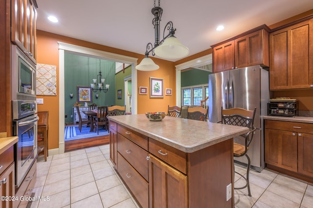 kitchen with light tile patterned floors, appliances with stainless steel finishes, a breakfast bar, a kitchen island, and decorative light fixtures