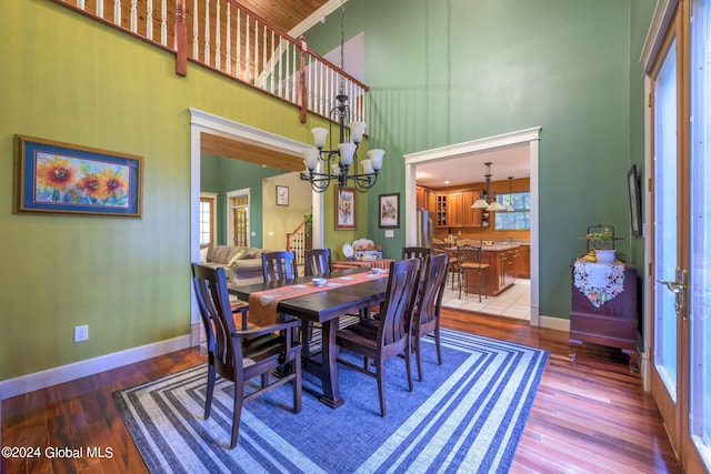 dining space featuring baseboards, wood finished floors, an inviting chandelier, and a high ceiling