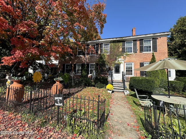 view of front facade with brick siding, fence, and a chimney