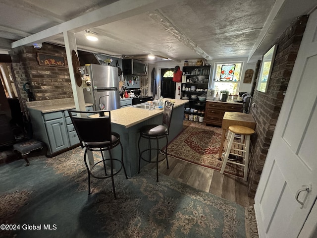 kitchen featuring appliances with stainless steel finishes, a kitchen island with sink, brick wall, a breakfast bar area, and dark wood-style floors