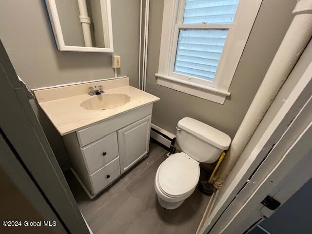 bathroom with wood-type flooring, vanity, baseboard heating, and toilet