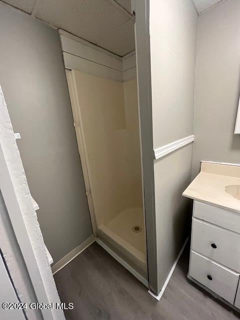 bathroom with a drop ceiling, hardwood / wood-style flooring, vanity, and a shower