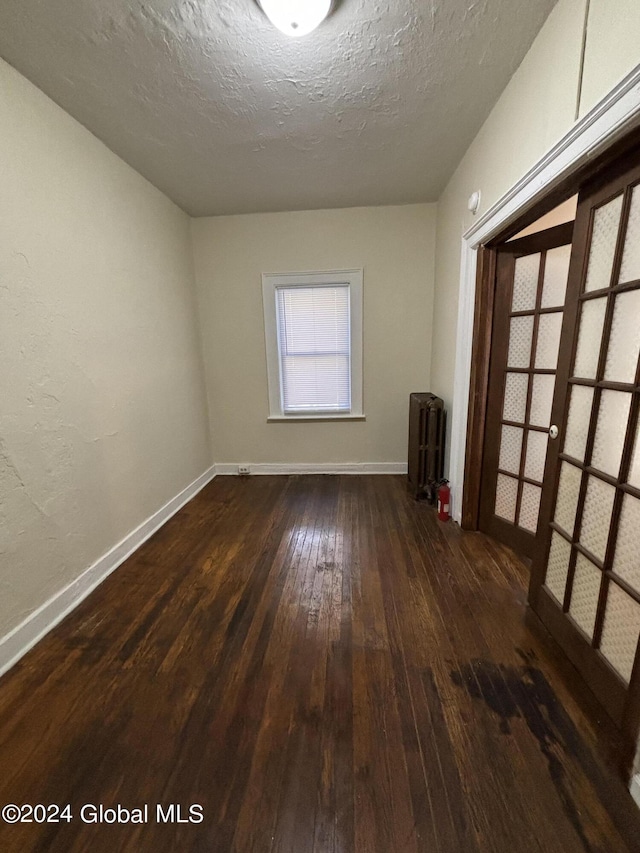 unfurnished room featuring dark wood-type flooring, a textured ceiling, radiator, and baseboards