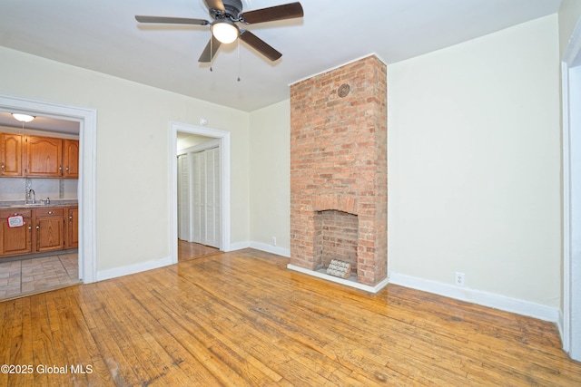 unfurnished living room with light wood-style floors, ceiling fan, a fireplace, a sink, and baseboards
