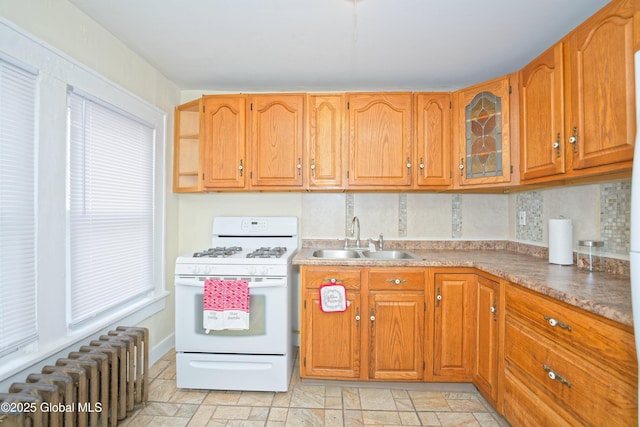 kitchen featuring tasteful backsplash, white gas range oven, radiator, stone finish flooring, and a sink