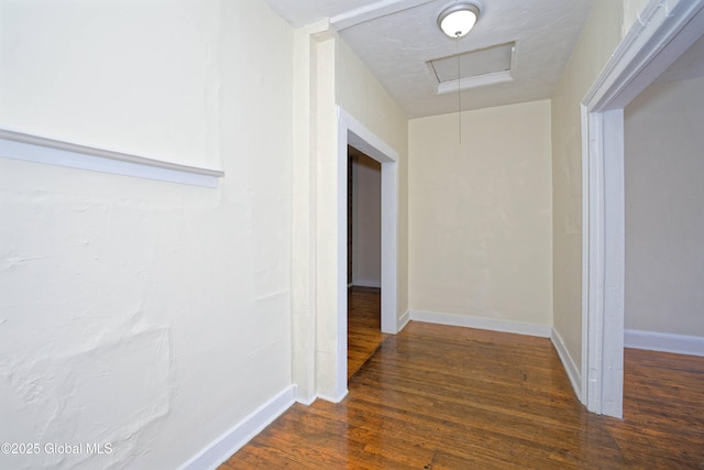 hallway with baseboards, attic access, and wood finished floors