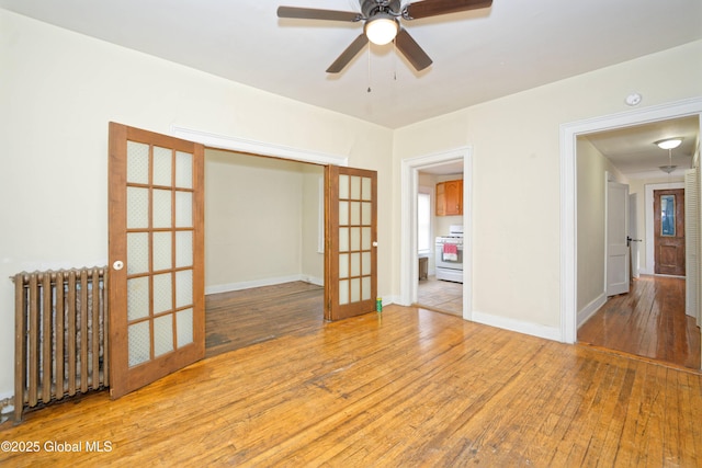 spare room with wood-type flooring, radiator heating unit, ceiling fan, and baseboards