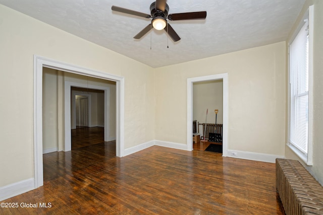 spare room featuring baseboards, a ceiling fan, a textured ceiling, wood finished floors, and radiator heating unit