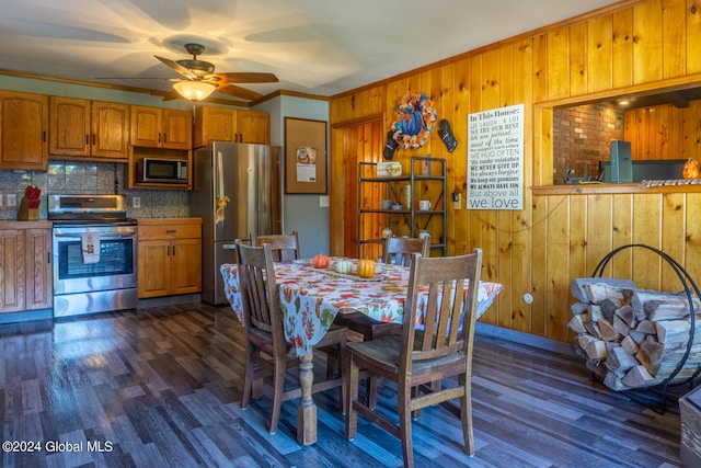 dining space featuring dark wood-type flooring, ceiling fan, wood walls, and crown molding