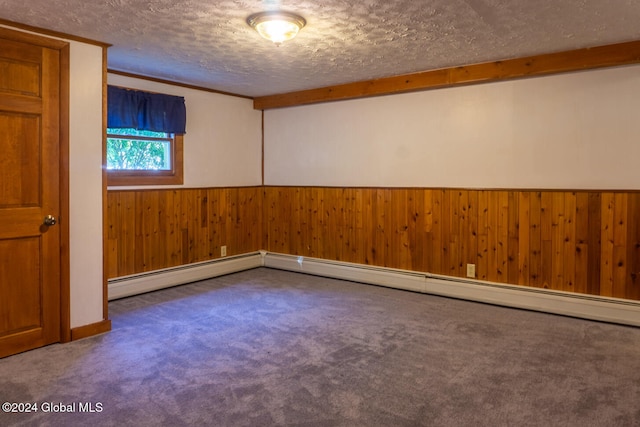 carpeted empty room featuring a baseboard heating unit, wood walls, and a textured ceiling