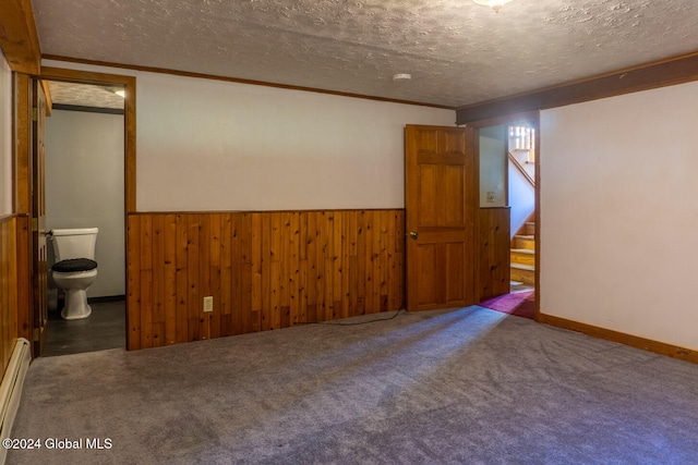 spare room featuring a baseboard heating unit, wood walls, a textured ceiling, carpet floors, and ornamental molding