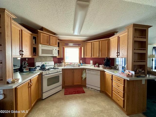 kitchen featuring white appliances, a textured ceiling, sink, and kitchen peninsula