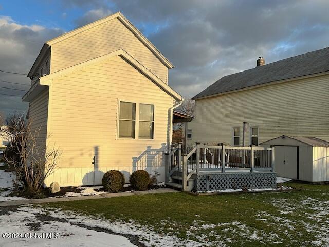 snow covered back of property with a storage shed, a lawn, and a deck