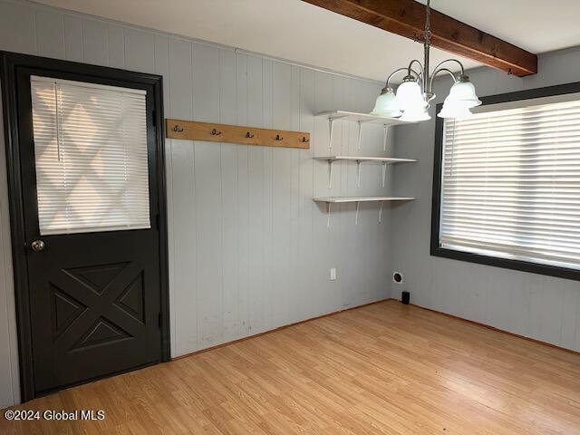 unfurnished dining area with an inviting chandelier, beam ceiling, wood walls, and light wood-type flooring