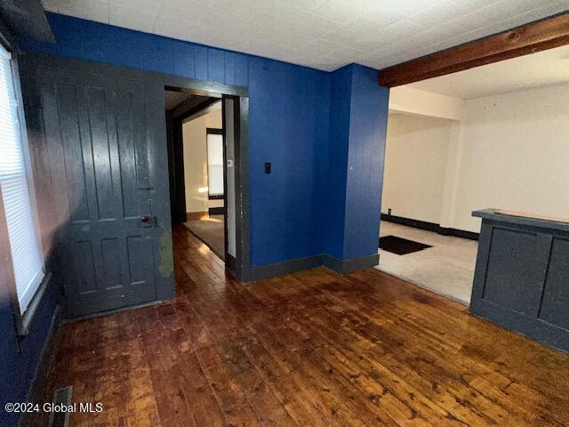 unfurnished room featuring beamed ceiling, dark wood-type flooring, and wooden walls